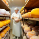 Woman wearing apron and hairnet standing in rows of fresh cheese